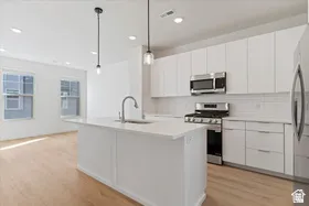 Modern kitchen featuring an island with an integrated sink, stainless steel appliances, white flat-panel cabinetry, a subway tile backsplash, and light wood-finish flooring
