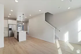 Open-concept living area featuring light wood-finish flooring, recessed lighting, a modern kitchen island with pendant lights, and a stainless steel refrigerator