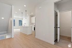 Open-concept living area featuring light wood-finish flooring, a white kitchen island with a built-in sink, and modern pendant lighting