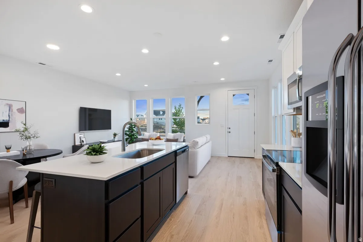 Open-concept kitchen featuring a large island with sink, stainless steel appliances, recessed lighting, and wood-finish flooring