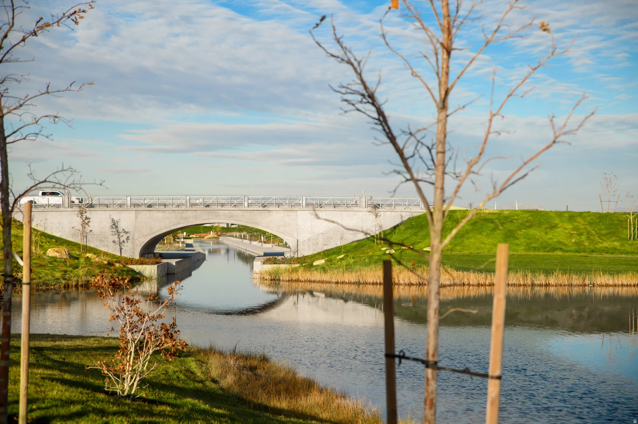 Waterway with an arched concrete bridge, surrounded by manicured green embankments and natural foliage