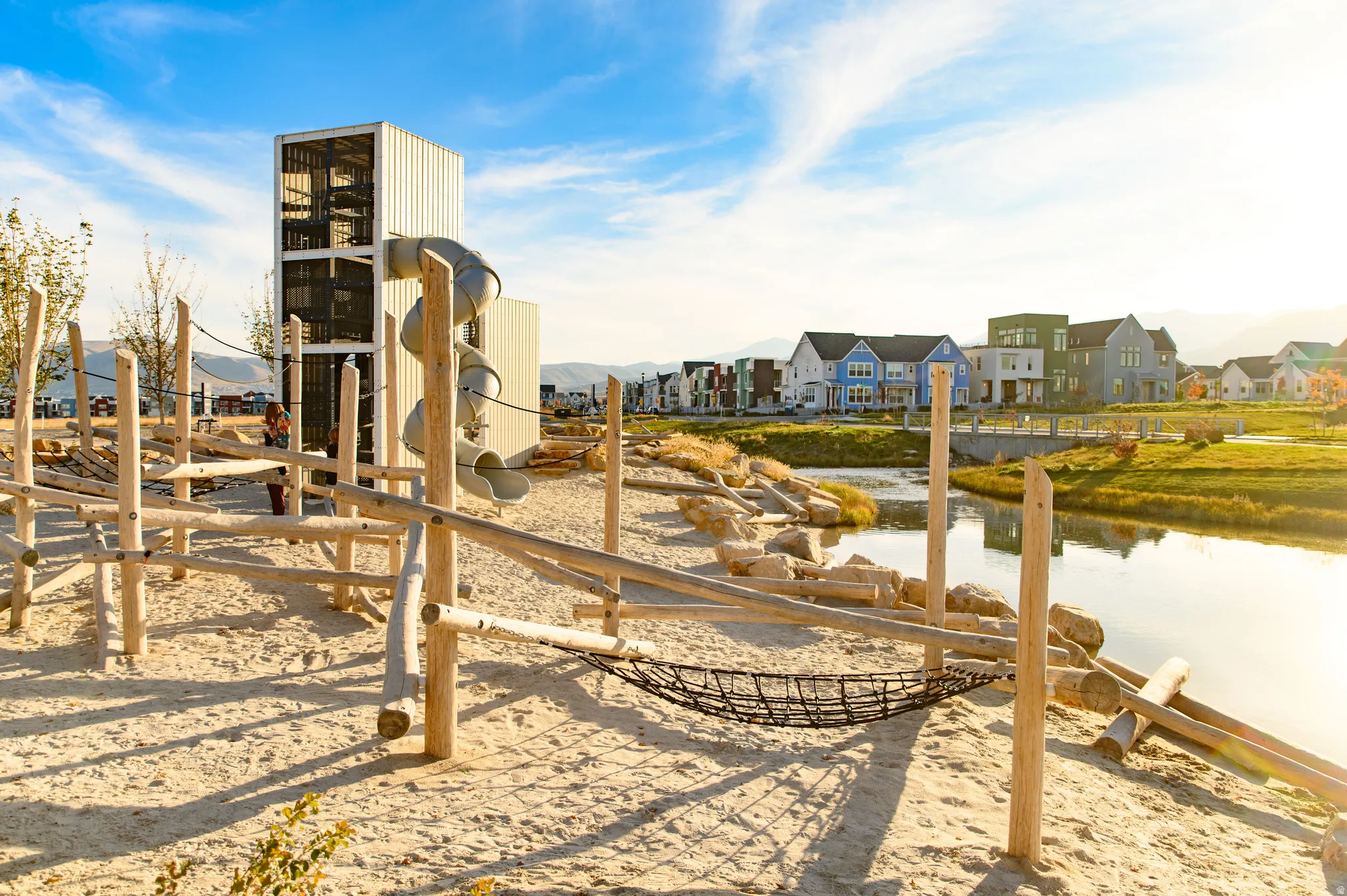 Expansive sand-covered recreation area featuring a multi-level climbing structure with a spiral slide, natural wood playground elements, and a net hammock