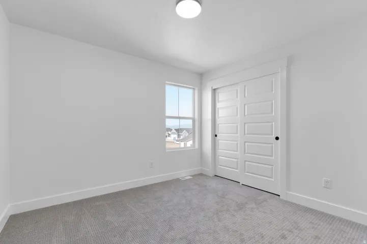Neutral white walls and trim, gray carpeted flooring, and a single window with a white frame