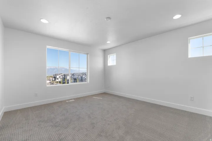 Recessed ceiling lighting, multiple windows, plush gray carpeting, white walls, and white trim