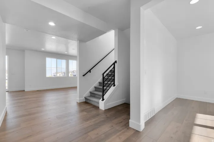 Wood-finish flooring throughout, recessed lighting, and a staircase with a black metal railing