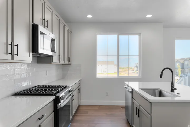 Modern kitchen featuring light gray cabinetry with black hardware, stainless steel appliances, white subway tile backsplash, and light-toned countertops