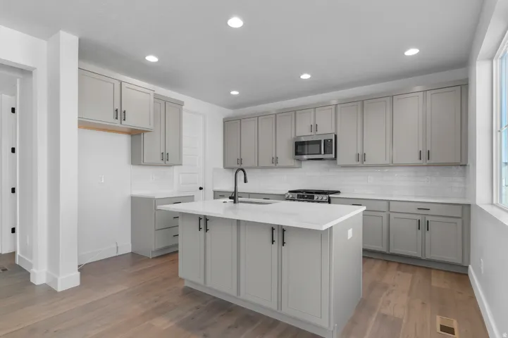 Kitchen featuring light gray cabinetry, white countertops, stainless steel appliances, a subway tile backsplash, and wood-finish flooring