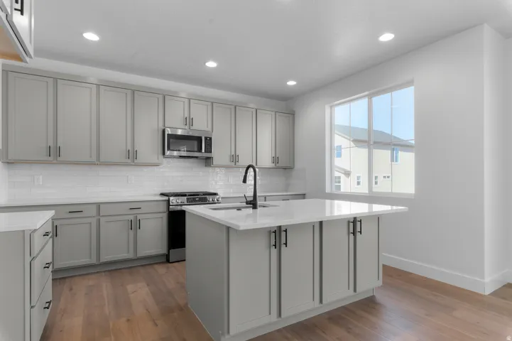 Kitchen featuring an island, light gray cabinetry, white countertops, stainless steel appliances, and wood-finish flooring