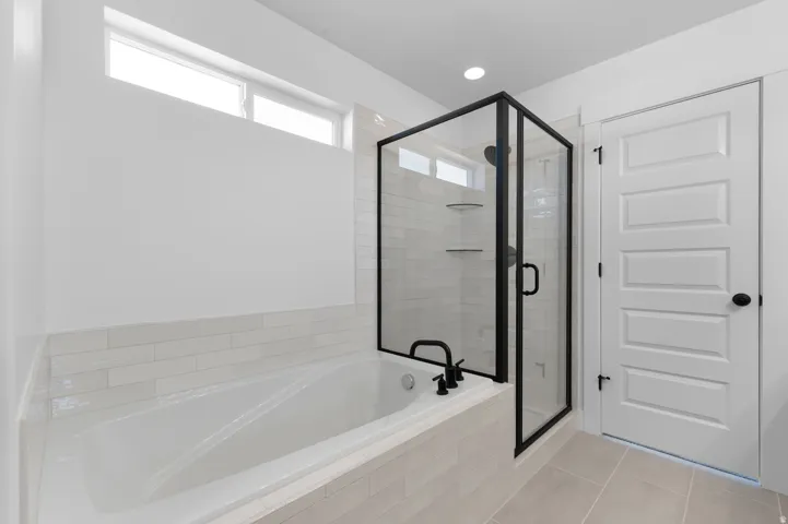 Freestanding soaking tub with matte black fixtures, enclosed shower with black-framed glass, white subway tile surround, and light-toned floor tiling