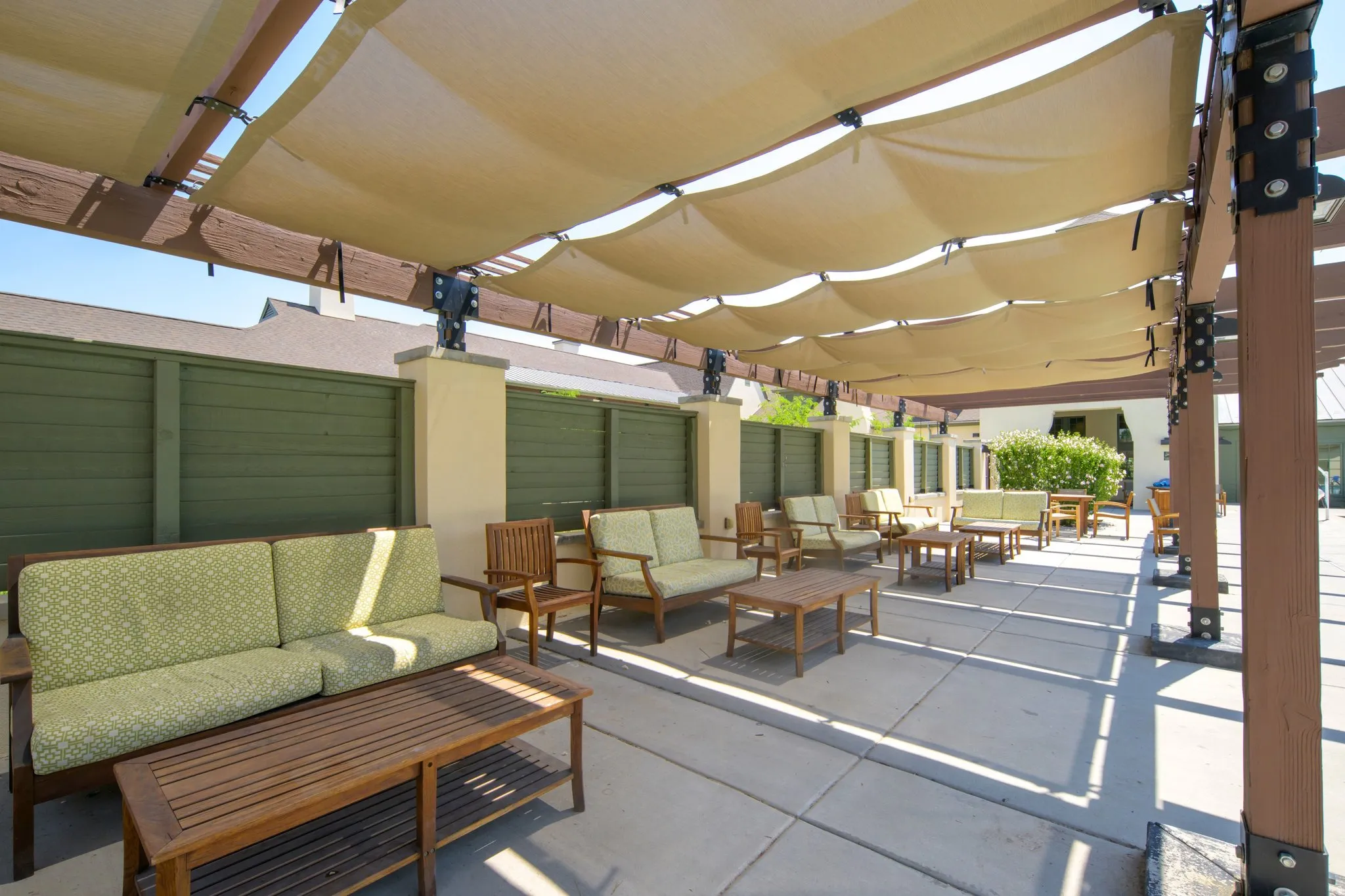 Expansive outdoor patio featuring a large shade structure with adjustable fabric canopies, concrete flooring, and decorative privacy fencing