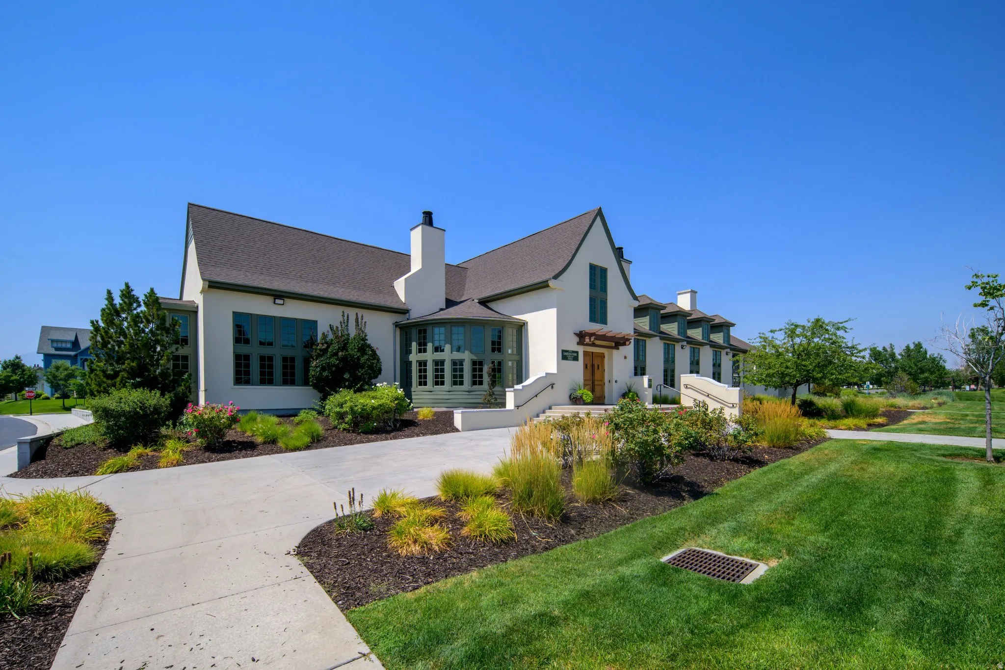 Stucco exterior with a pitched roofline, multiple chimneys, a curved driveway, and established landscaping