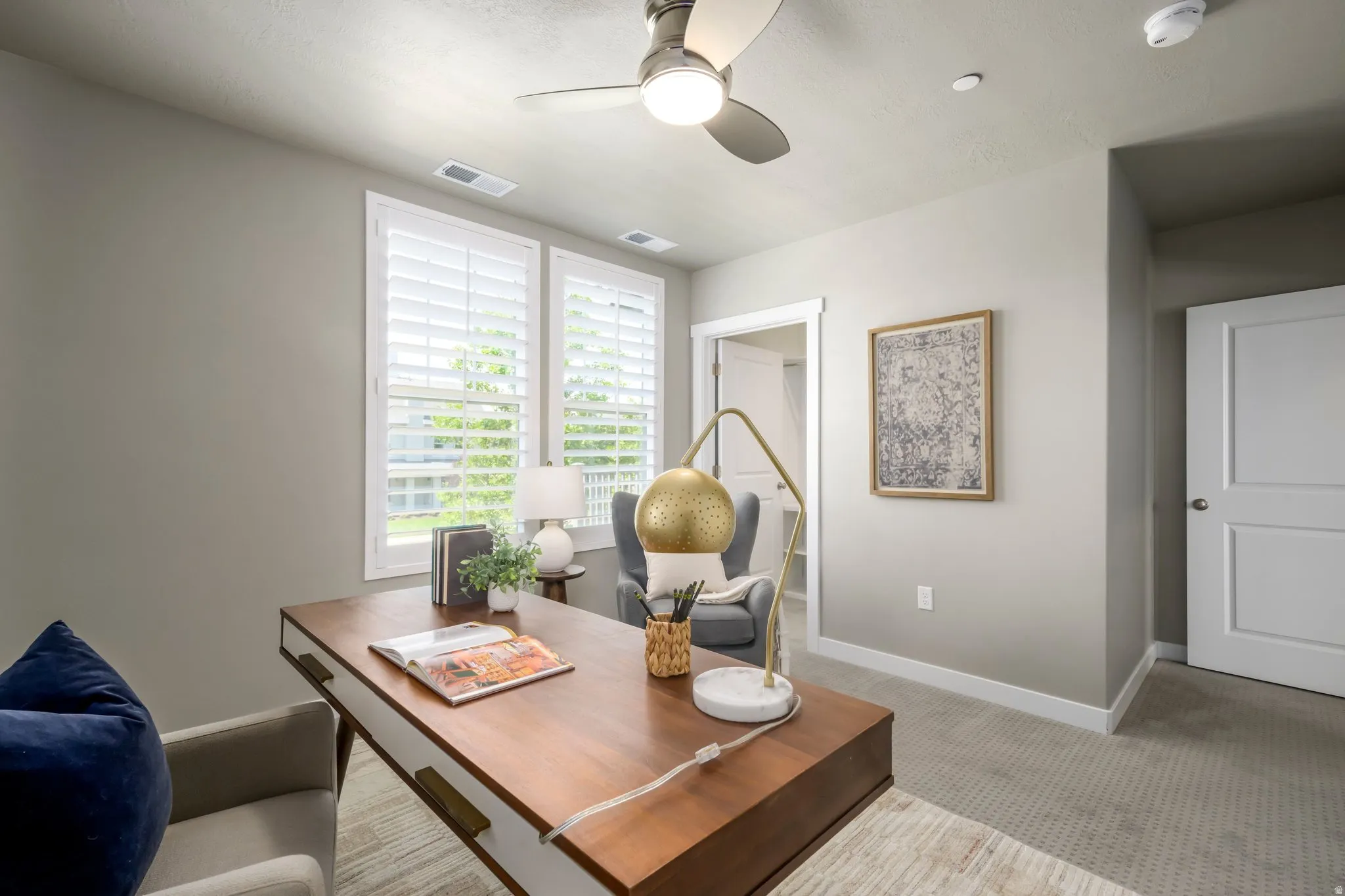 Room featuring two windows with white plantation shutters, neutral-toned walls, and a ceiling fan with integrated lighting