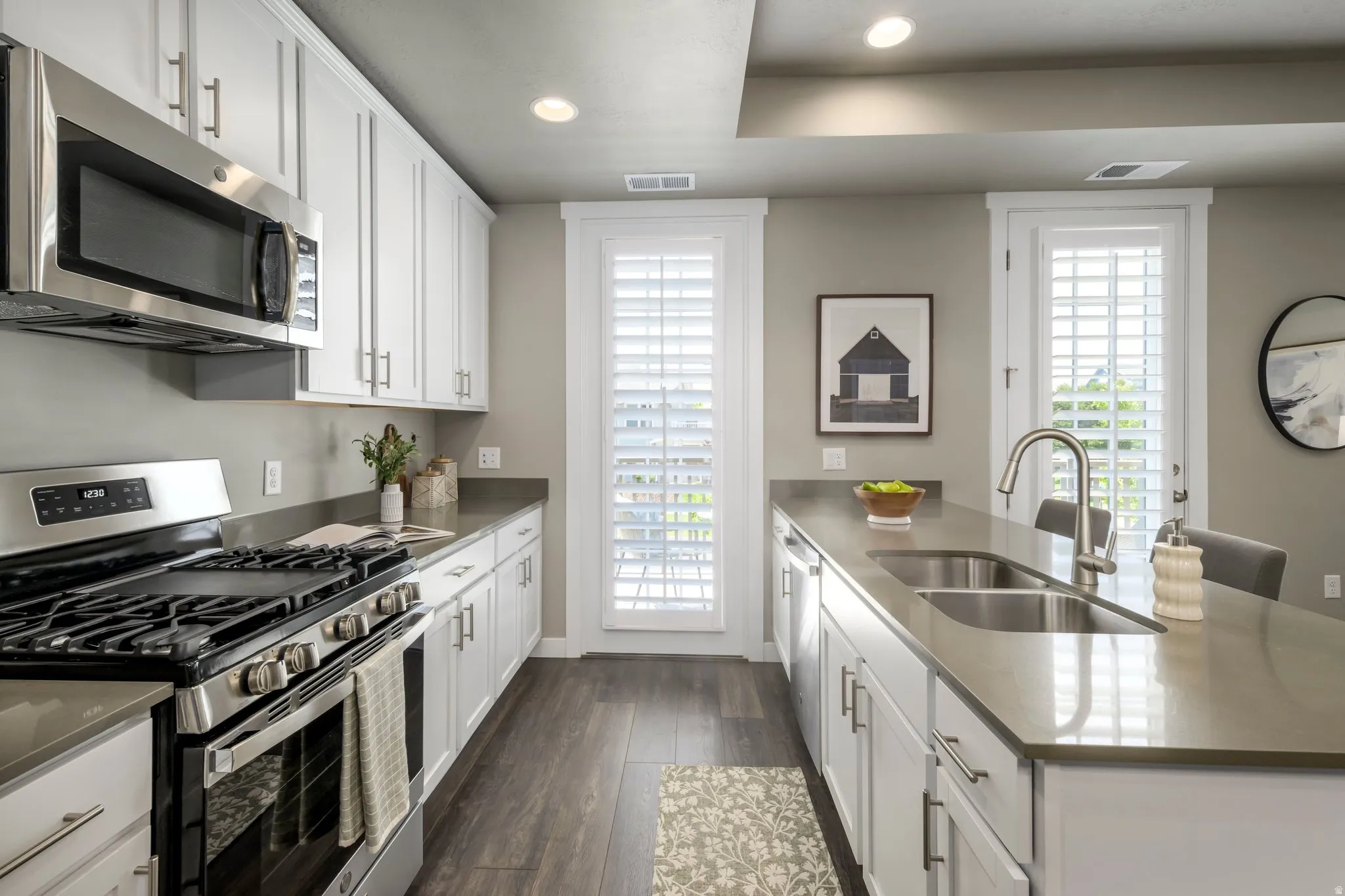 Gourmet kitchen with stainless steel appliances, white cabinetry, solid surface countertops, a double basin undermount sink, and wood-finish flooring