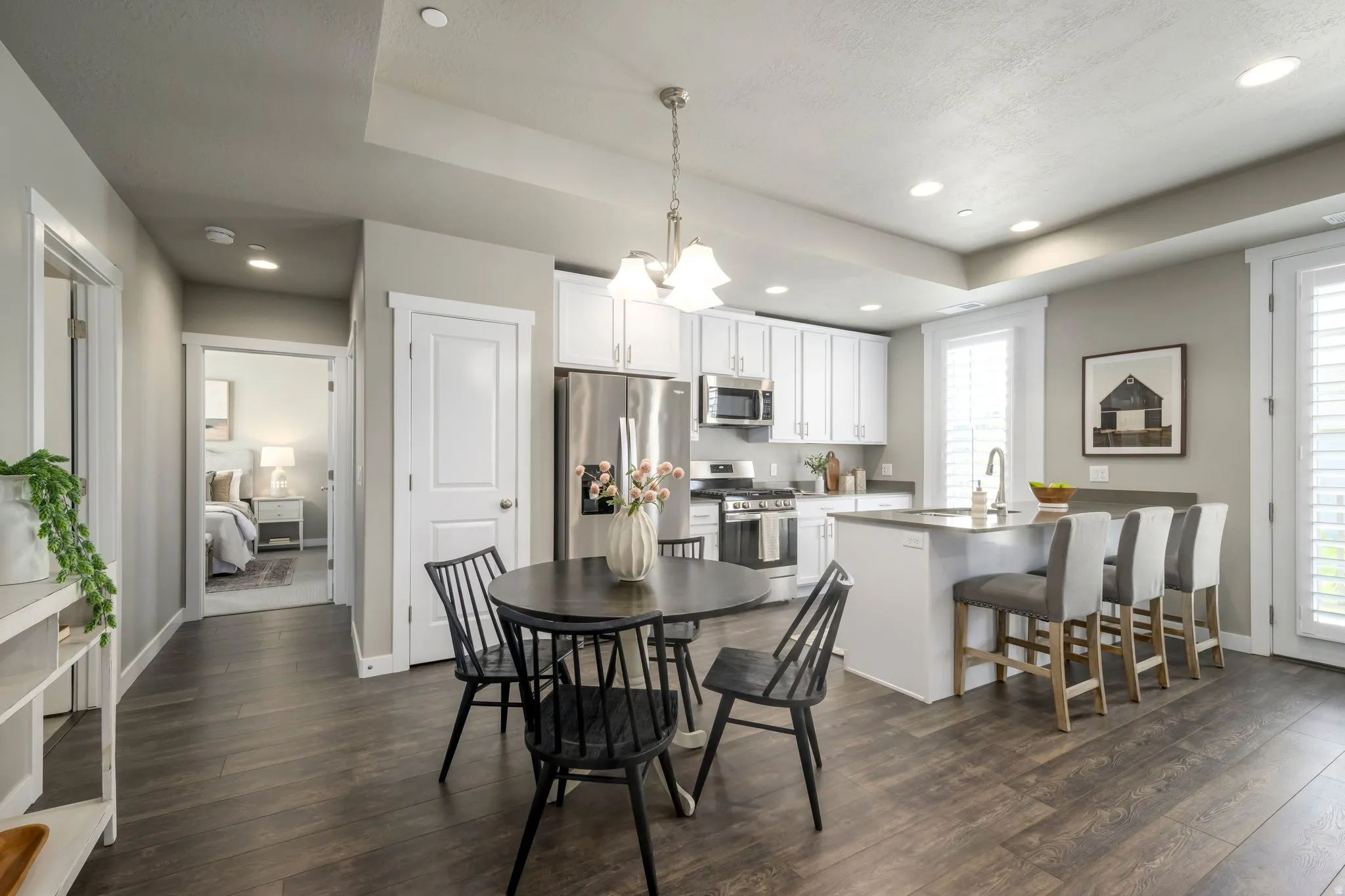 Open concept kitchen featuring white cabinetry, stainless steel appliances, a center island with seating, and wood-finish flooring