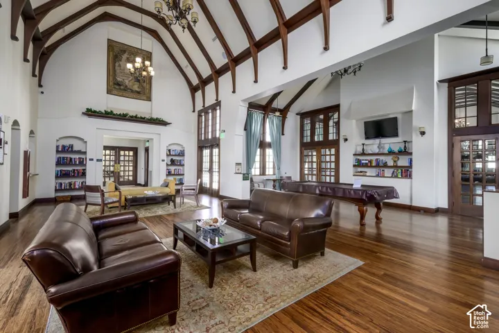 Spacious common area featuring vaulted ceilings with exposed wood beams, wood-finish flooring, built-in shelving, and multiple large windows with transom details