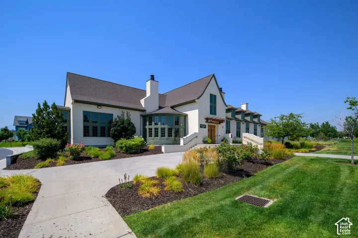 Stucco exterior with a pitched roofline, multiple chimneys, a curved driveway, and established landscaping