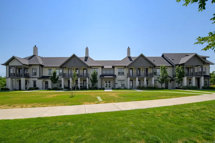 Multi-unit residential structure featuring a light-toned exterior with dark gray gables and balconies