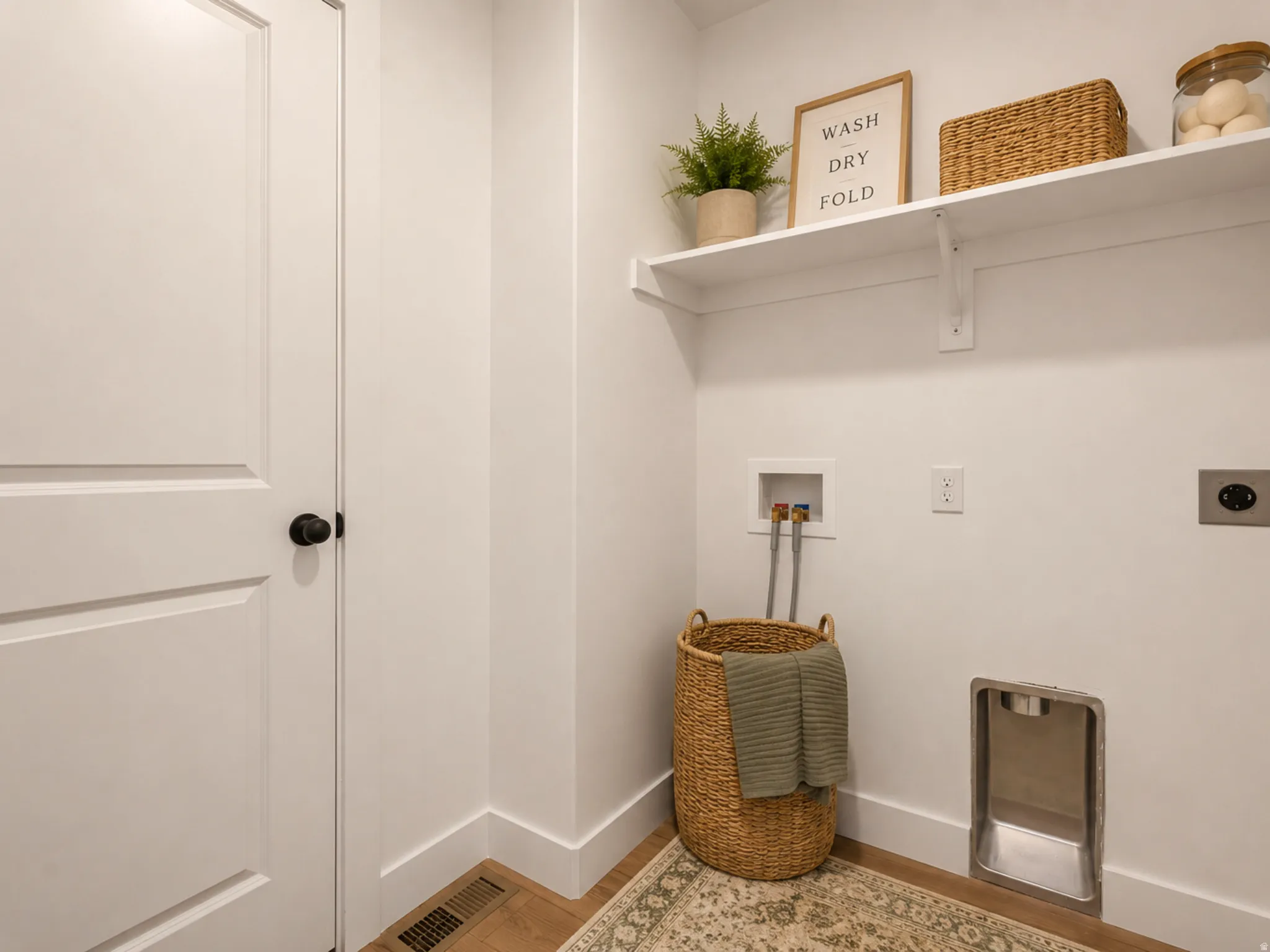 Dedicated laundry area featuring a white wall shelf, utility hookups, and wood-finish flooring