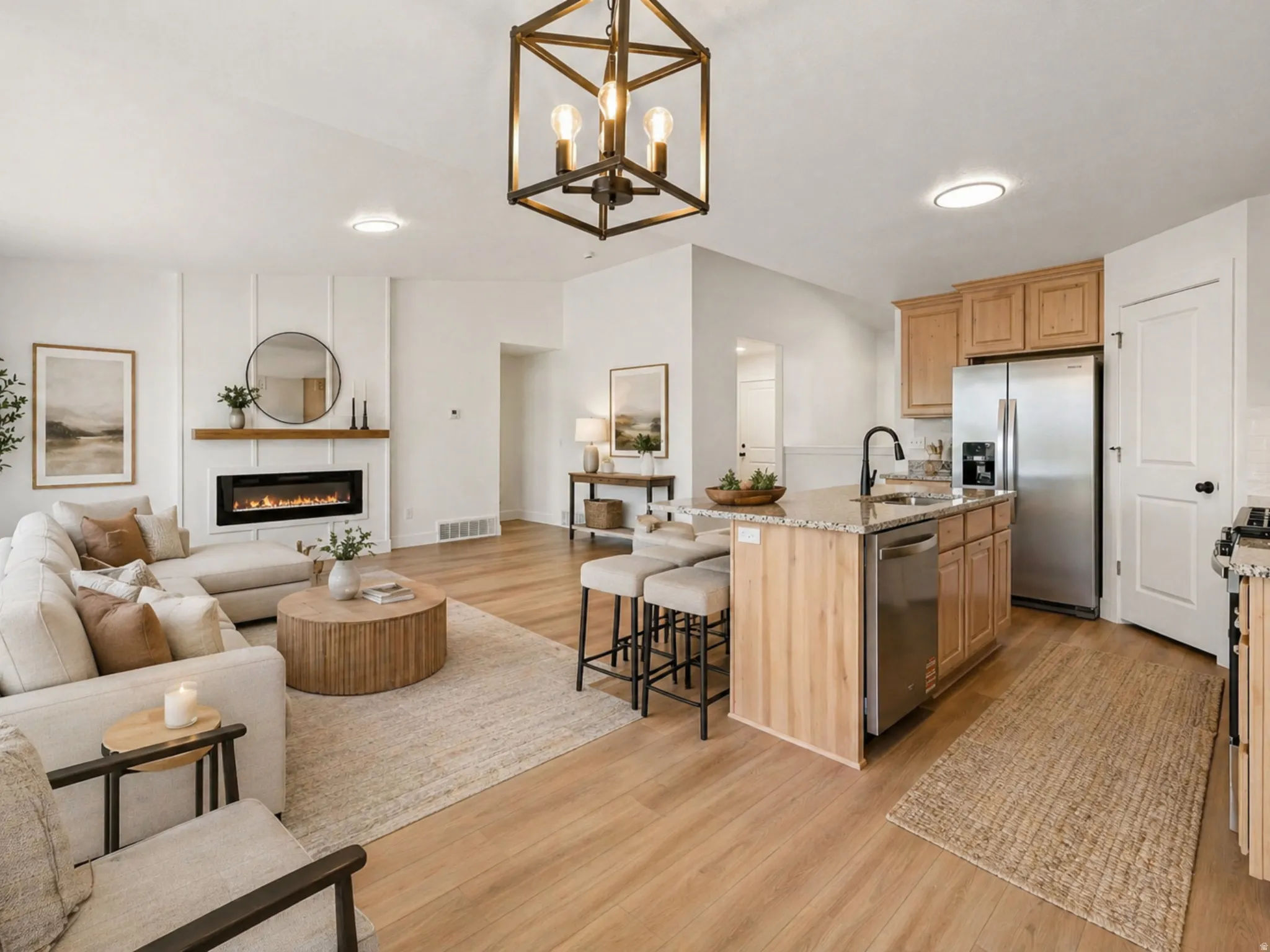 Open-concept living space featuring wood-finish flooring, a contemporary fireplace with a wood mantel, and a kitchen island with a stone-finish countertop