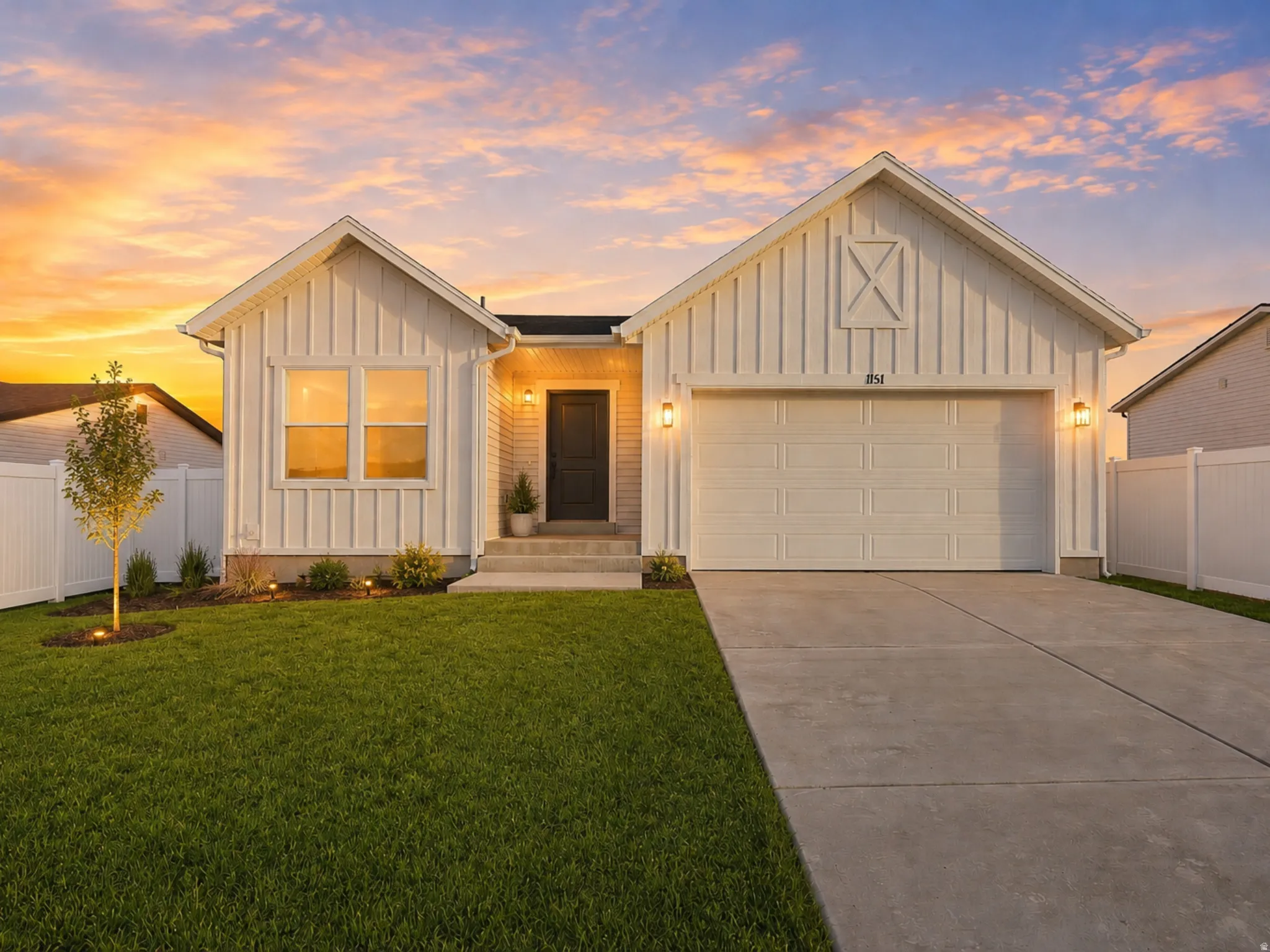White board and batten exterior featuring a two-car garage, dark front door, concrete driveway, front lawn, and white privacy fencing