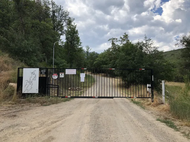 Black metal privacy gate with reflective red and white strips, positioned at the entrance of a gravel drive