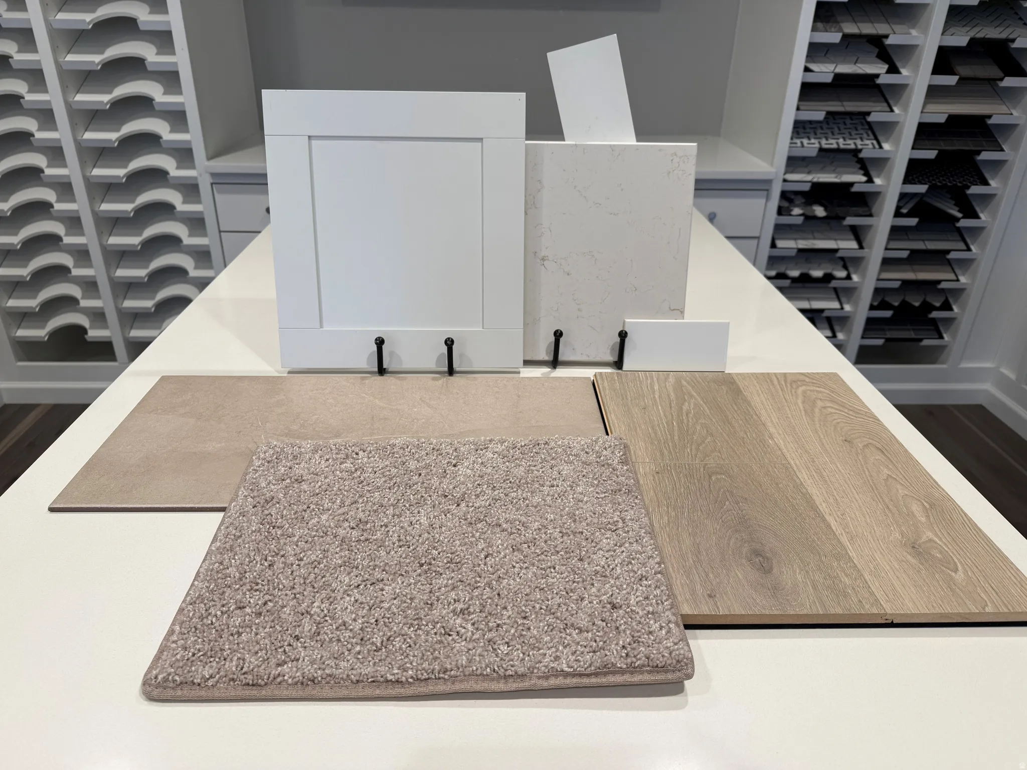 White shaker cabinet door with matte black pulls, light-toned wood-finish flooring, and a textured beige carpet sample