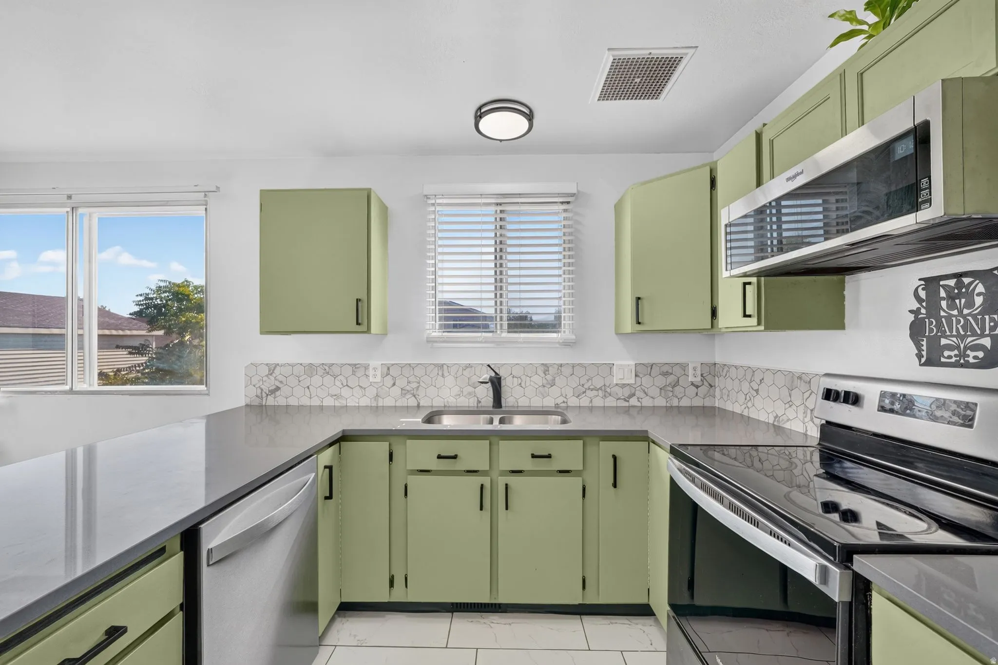 Kitchen featuring sage green cabinetry, dark countertops, a stainless steel over-the-range microwave, and a hexagon-patterned backsplash