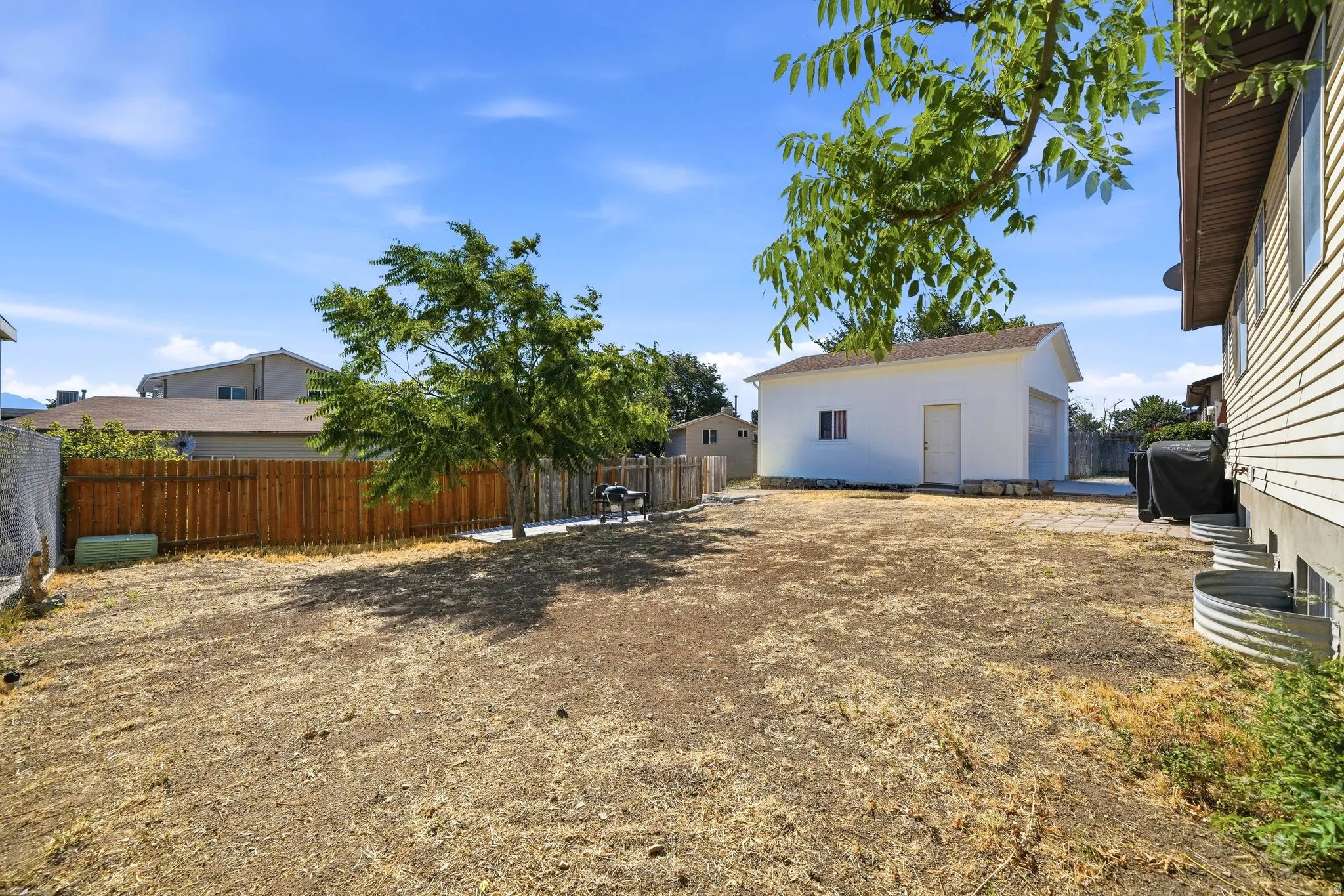 Expansive backyard featuring a detached garage with a roll-up door, a wooden privacy fence, mature trees, and a concrete patio