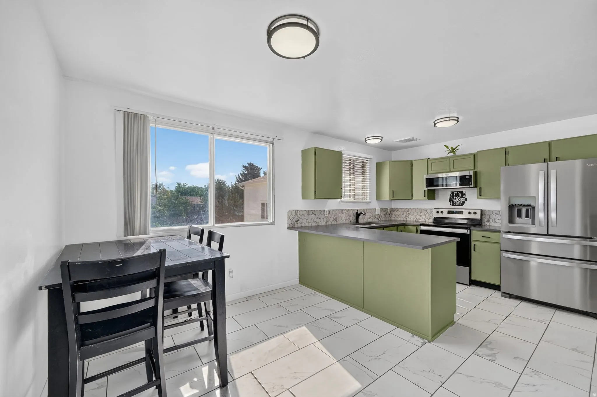 Kitchen featuring sage green cabinetry, stainless steel appliances, a center island with counter seating, and white tile flooring