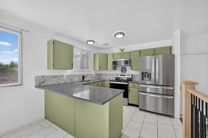 Modern kitchen featuring green cabinetry, stainless steel appliances, and a tiled backsplash