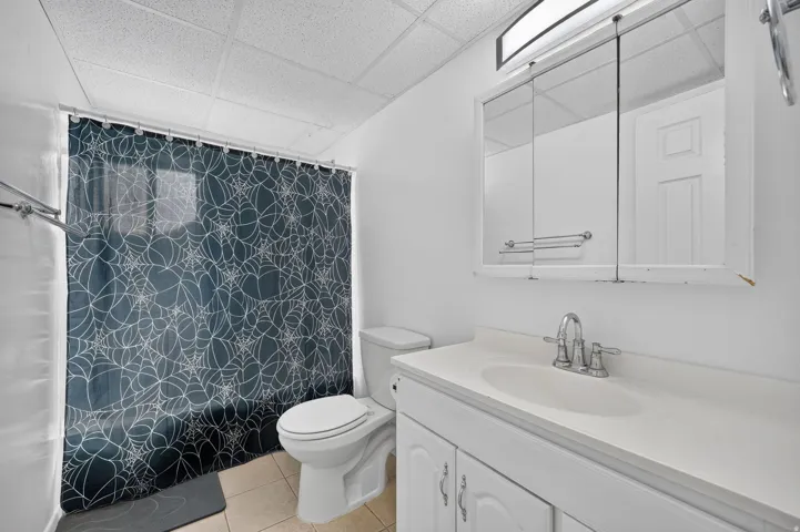 Bathroom featuring a drop ceiling, tile flooring, a white vanity with an integrated sink, a mirrored medicine cabinet, and a chrome faucet