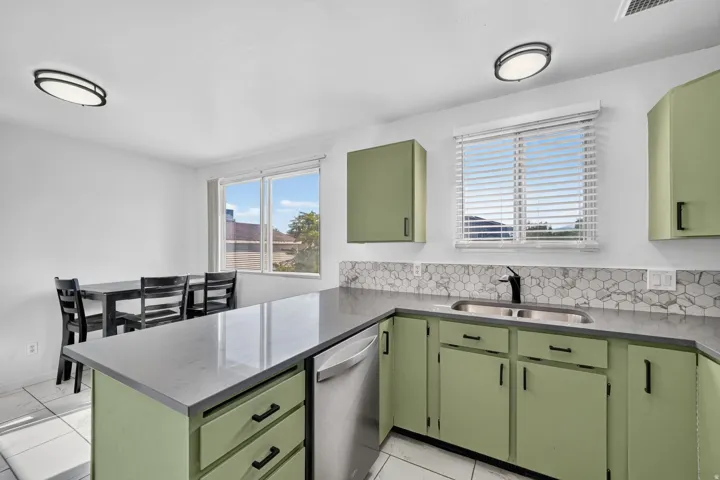 Kitchen featuring light green cabinetry, grey countertops, stainless steel dishwasher, and a hexagonal tile backsplash