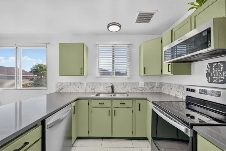 Kitchen featuring sage green cabinetry, dark countertops, a stainless steel over-the-range microwave, and a hexagon-patterned backsplash