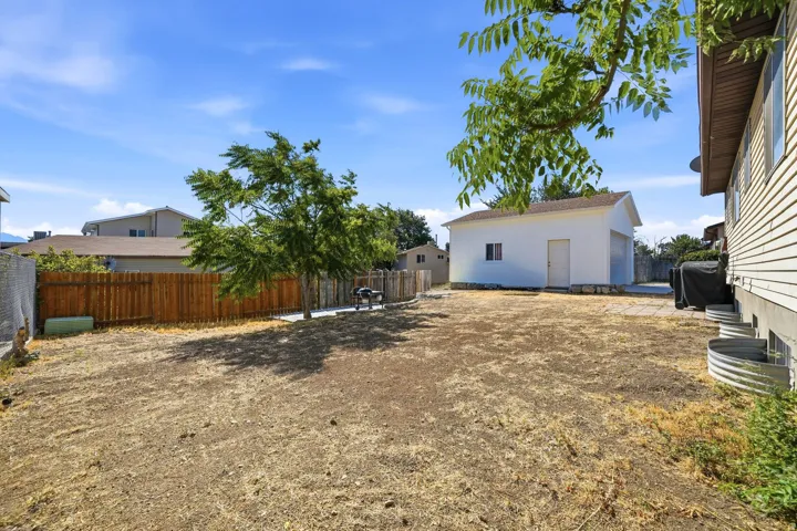 Expansive backyard featuring a detached garage with a roll-up door, a wooden privacy fence, mature trees, and a concrete patio