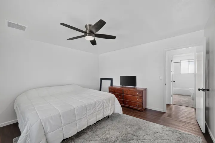 Bedroom featuring dark wood-finish flooring, white walls, and a contemporary ceiling fan with integrated lighting