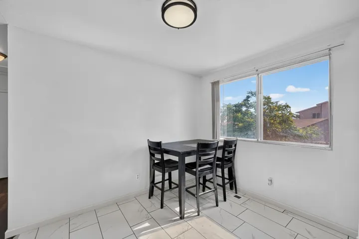 Bright interior space featuring large window, white walls, light tile flooring, and a flush mount ceiling light