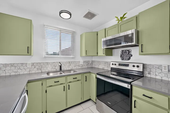 Kitchen featuring green cabinetry, gray countertops, and a white hexagonal tile backsplash