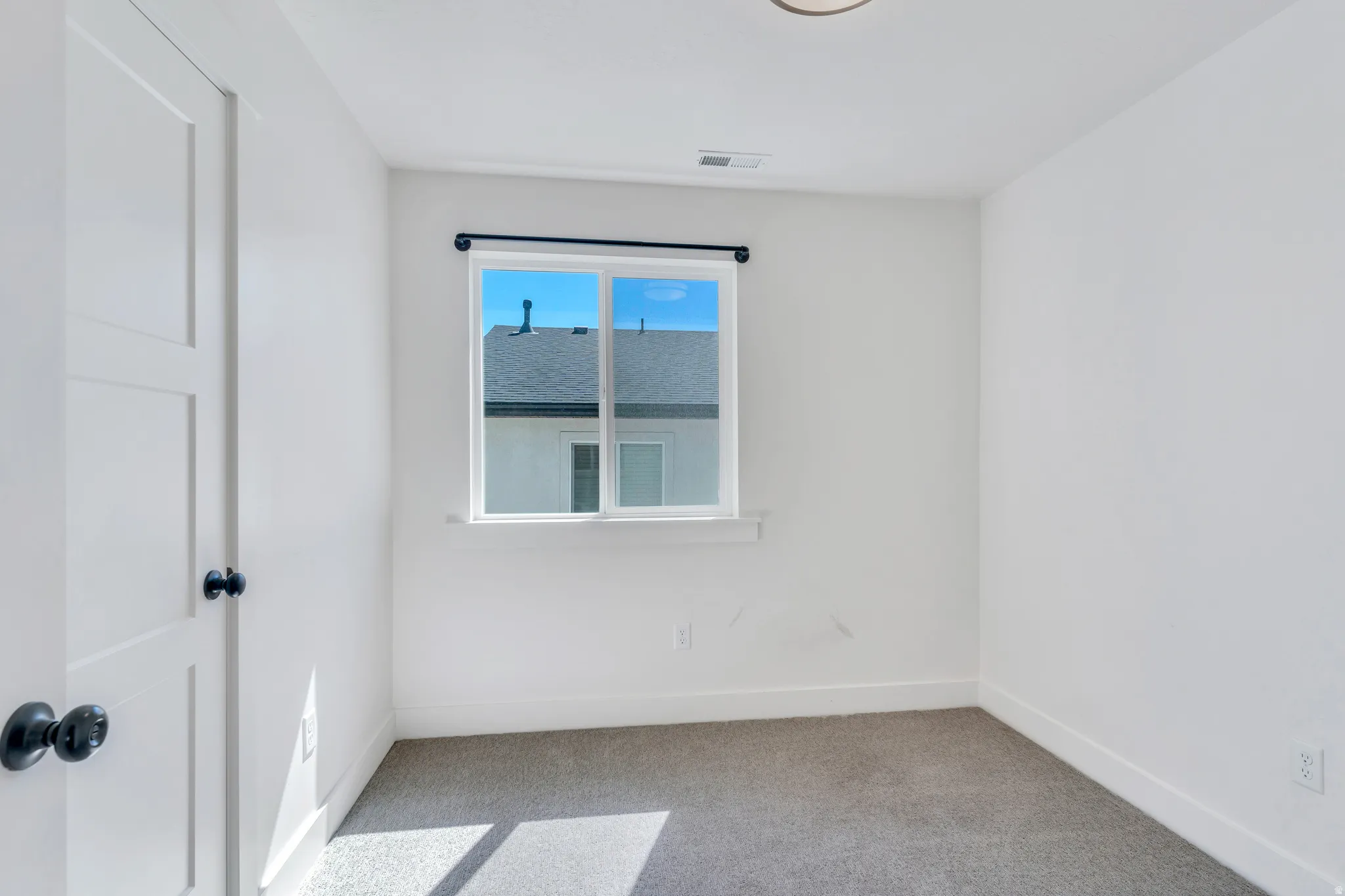 Bright interior space featuring a window with a black curtain rod, white walls, and light-colored carpeting