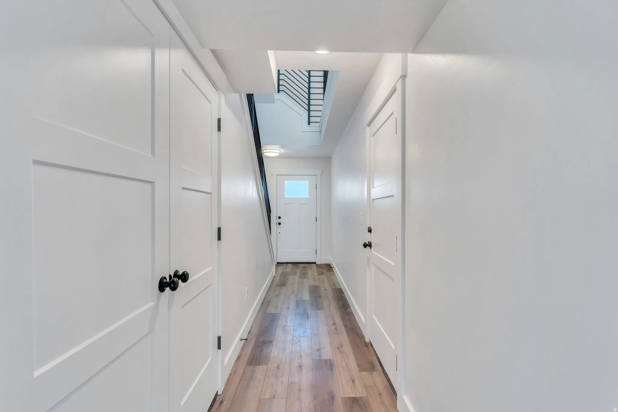 Hallway with wood-finish flooring, white panel doors, and contrasting black hardware