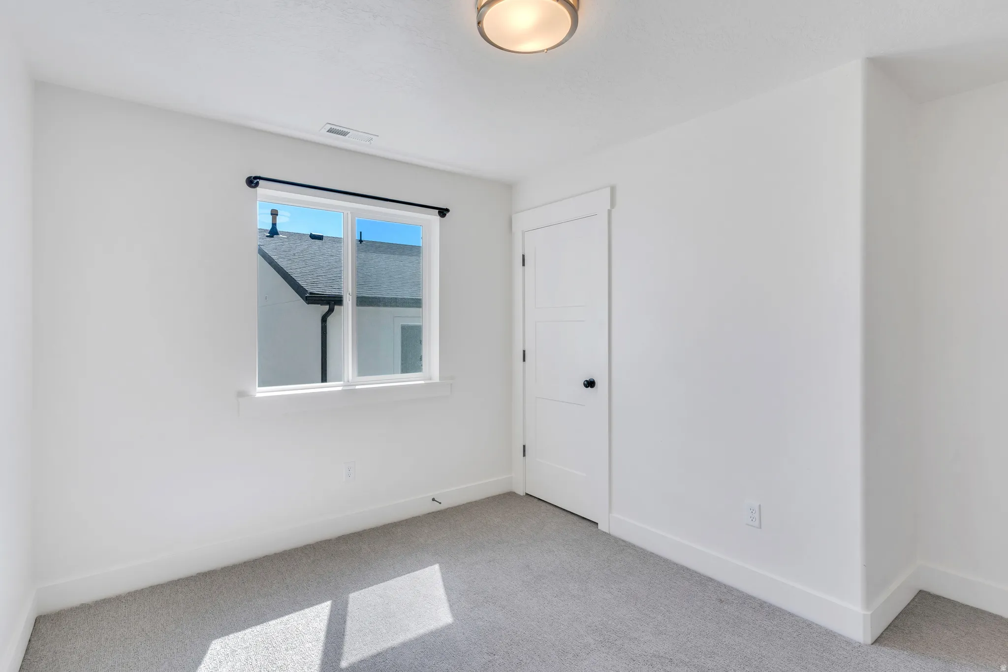 Bright interior space featuring a window with a black curtain rod, white walls, and light-colored carpeting