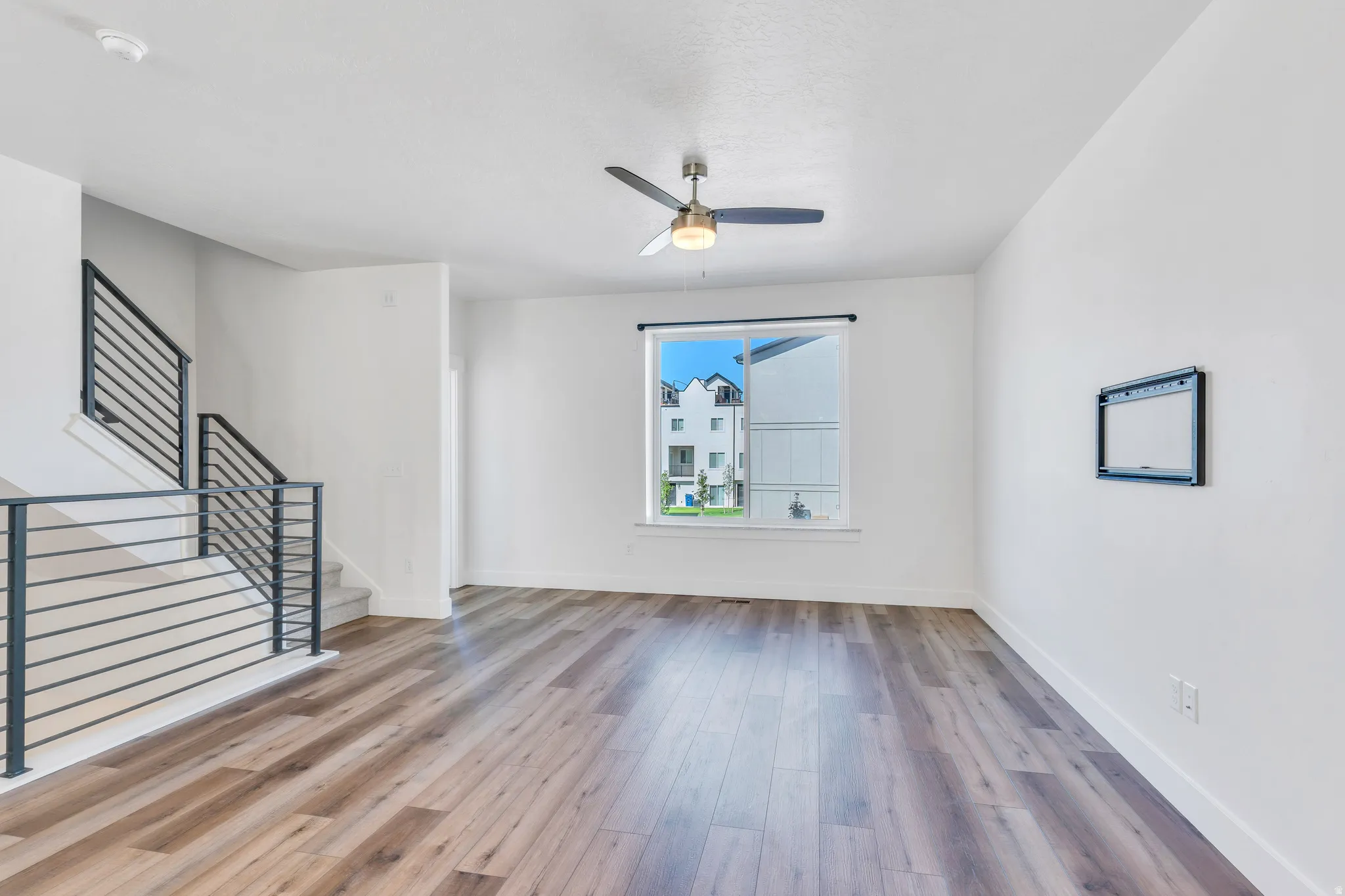 Spacious living area featuring wood-finish flooring, a contemporary ceiling fan, and a large window
