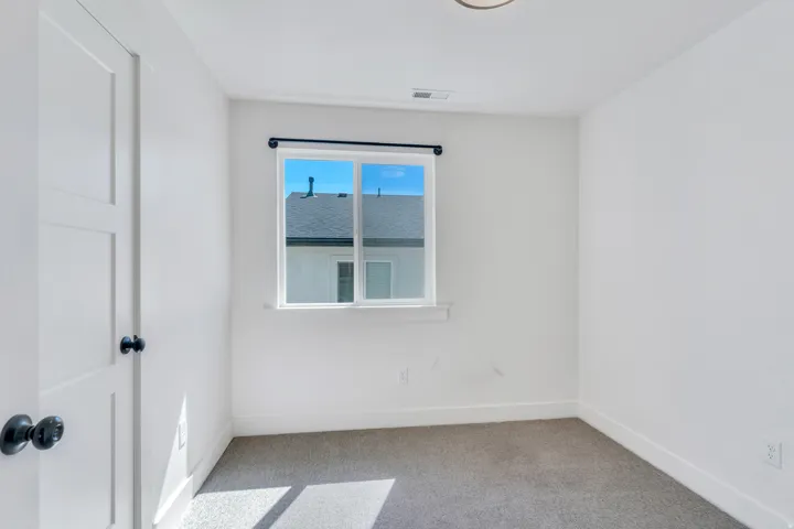 Bright interior space featuring a window with a black curtain rod, white walls, and light-colored carpeting