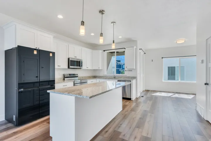 Modern kitchen featuring white cabinetry, granite countertops, wood-finish flooring, stainless steel appliances, and a central island with pendant lighting