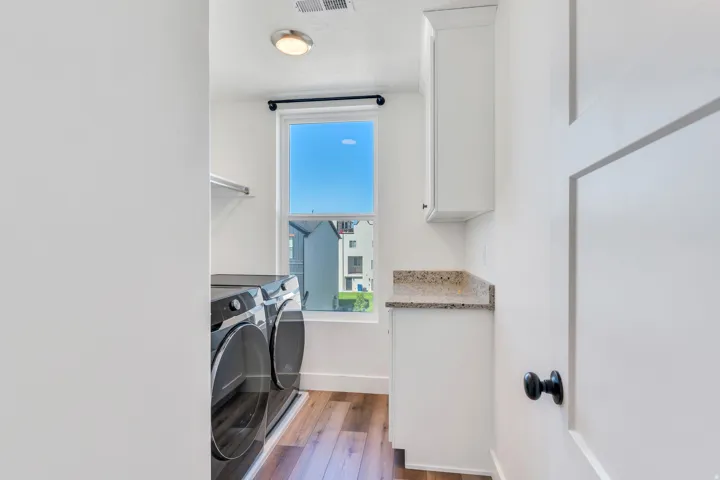 Laundry area featuring a window, wood-finish flooring, white cabinetry, a light-toned speckled countertop, and a built-in shelf