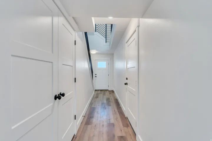 Hallway with wood-finish flooring, white panel doors, and contrasting black hardware