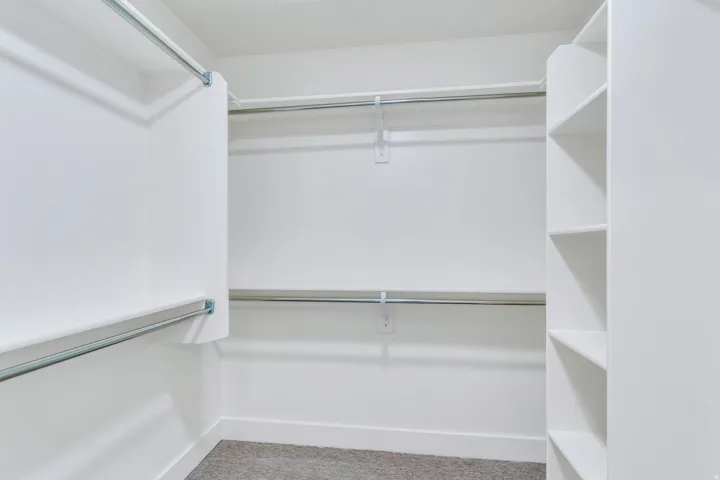 Walk-in closet featuring white built-in shelving, multiple hanging rods, white baseboards, and carpet flooring