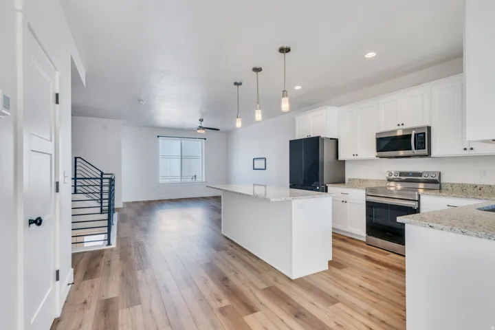 Open concept living area featuring wood-finish flooring, a contemporary kitchen island with pendant lighting, white cabinetry, stainless steel appliances, and a modern stair railing