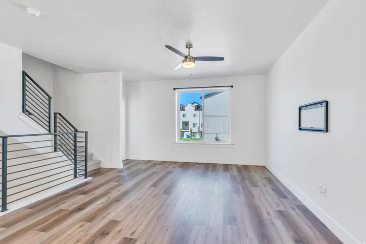 Spacious living area featuring wood-finish flooring, a contemporary ceiling fan, and a large window