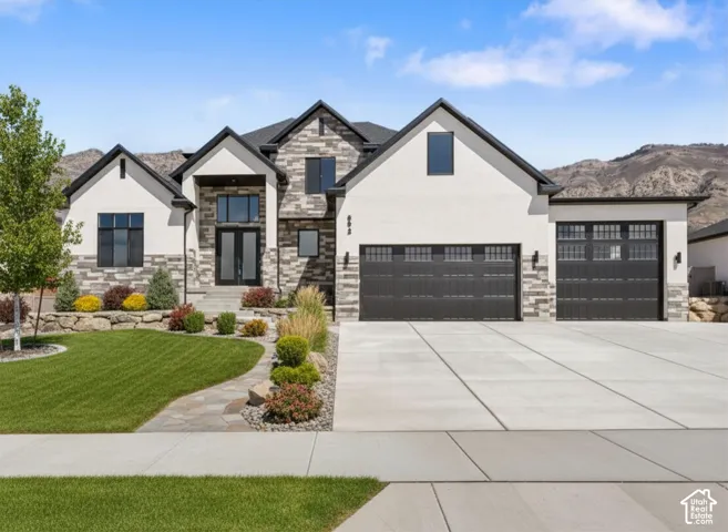 Contemporary residence featuring a stucco and stone facade, dark-frame windows, a prominent two-car garage, an additional single-car garage, and a concrete driveway