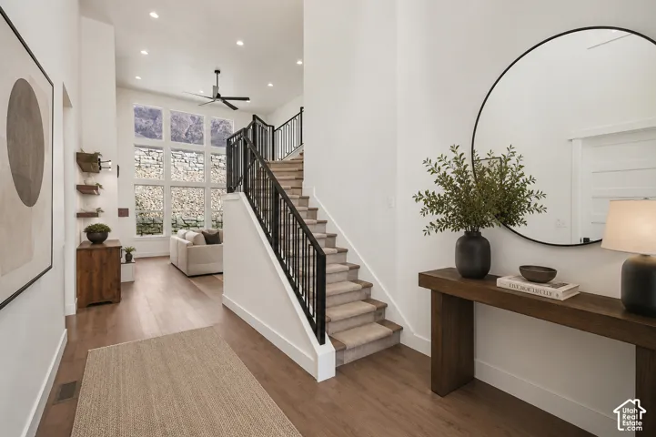Two-story entryway featuring wood-finish flooring, a carpeted staircase with black metal railings, and a multi-pane window wall